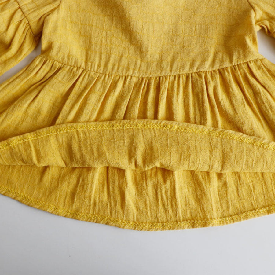 Detailed view of the cute designs on a baby girl’s yellow shirt.